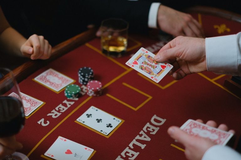 poker dealer deals card at red felt casino table